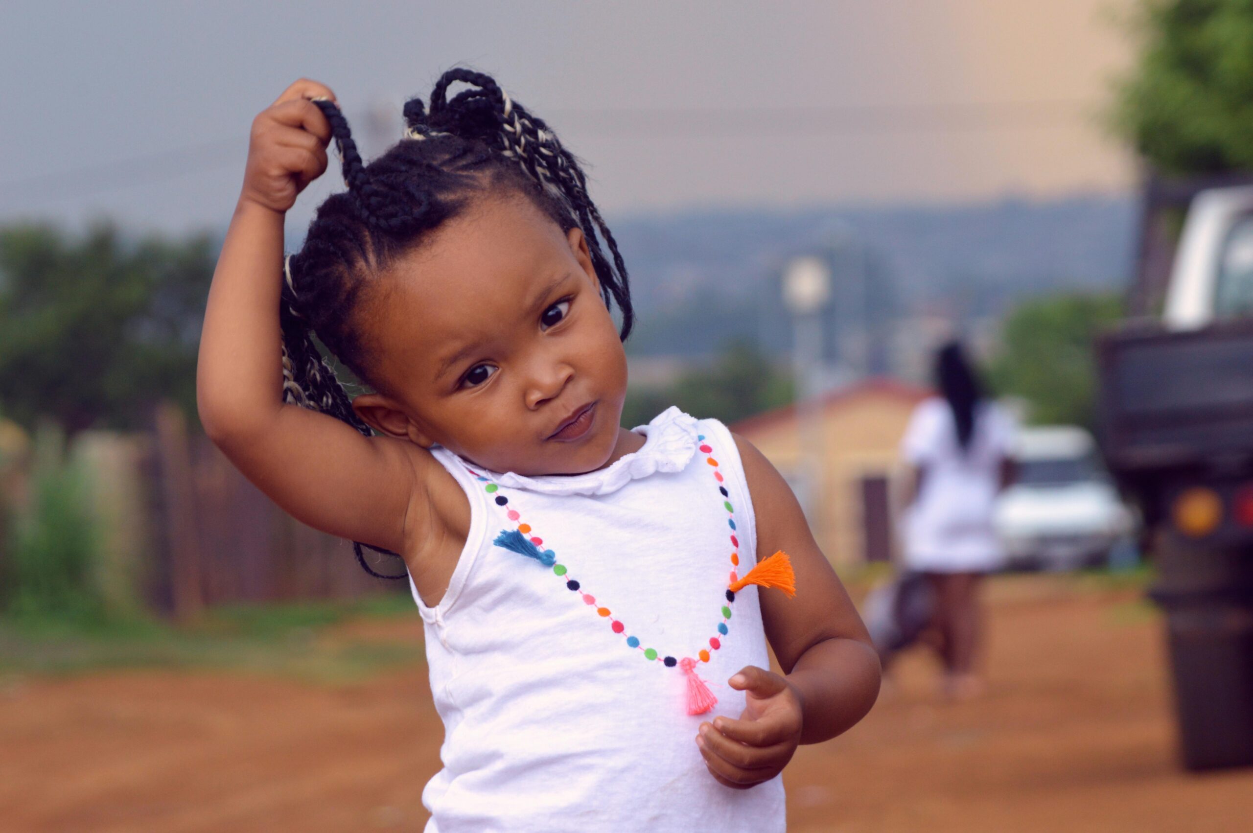 Cute child portrait with braided hair standing on a sunny day in a colorful necklace.